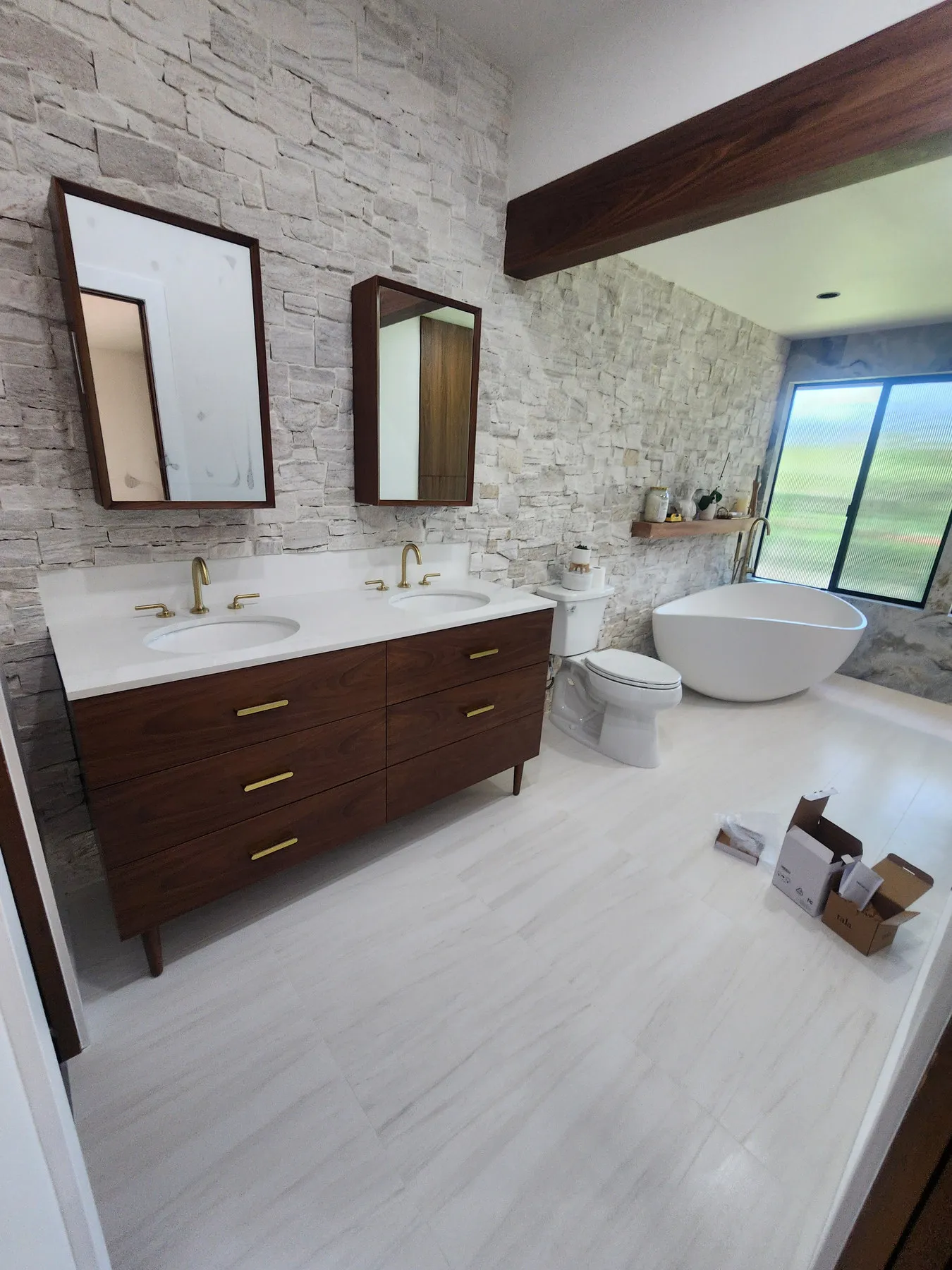 A light oak double vanity with a stone top and a lit mirror above it