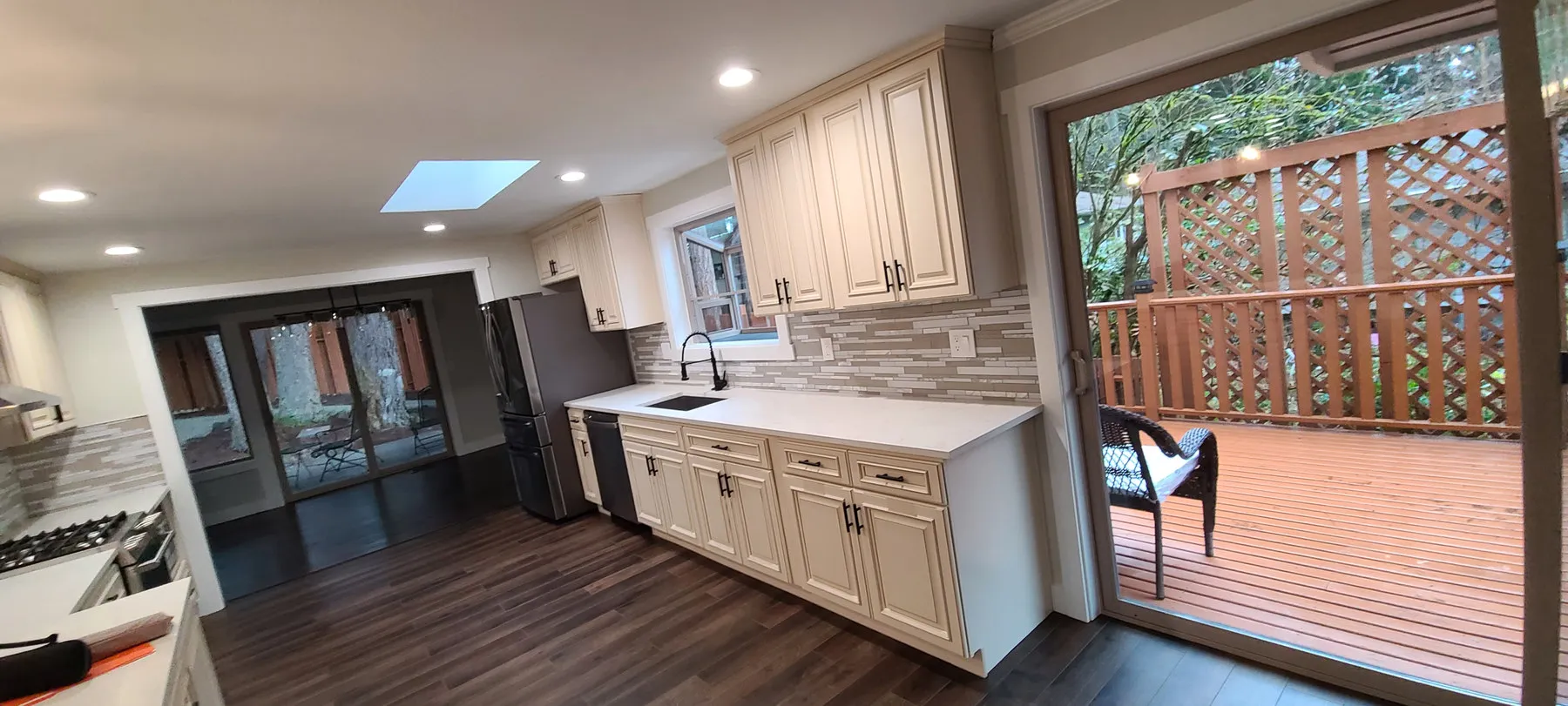A finished kitchen with cream shaker cabinets, quartz counters and a mosaic backsplash, looking out onto a deck
