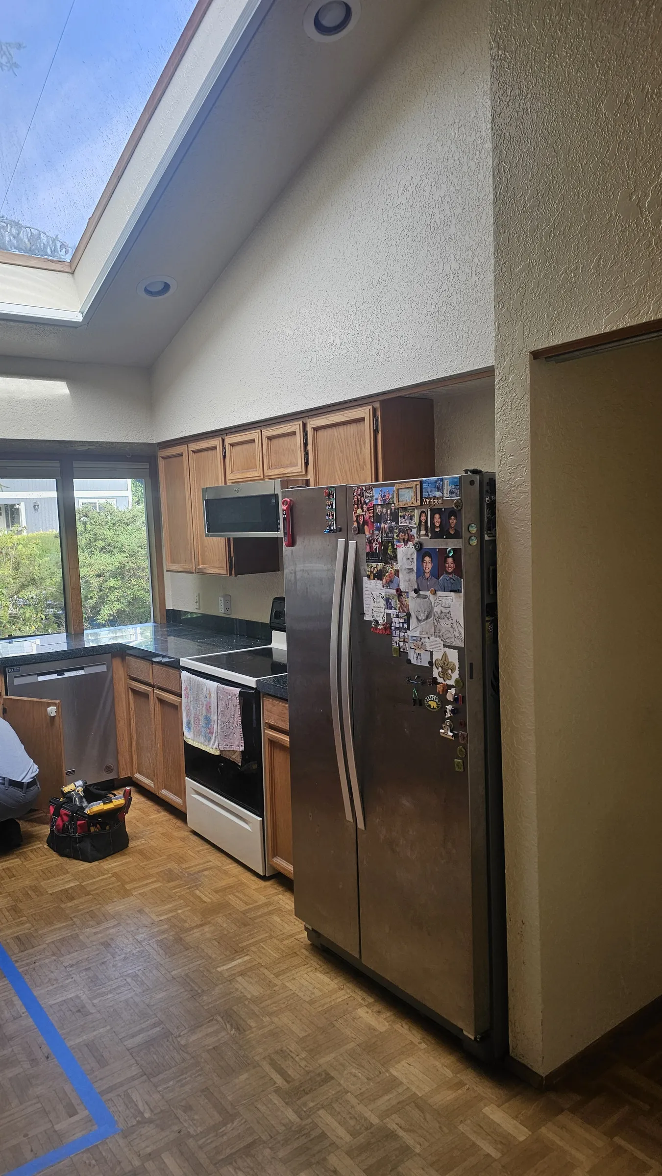 Before — A galley kitchen before and after renovation, oak cabinets and parquet replaced with sage-green shaker, a quartz island and wood flooring