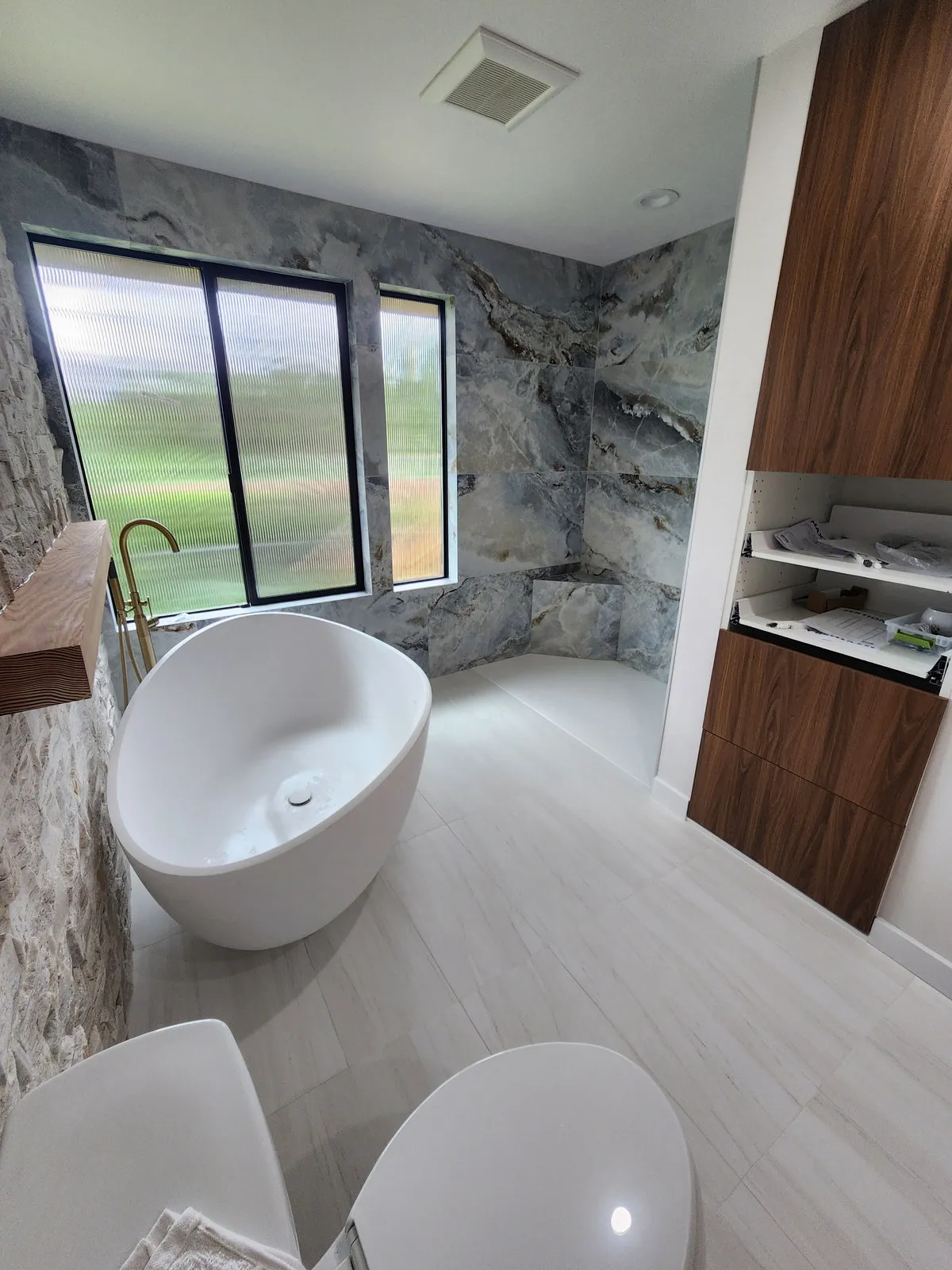 A finished bathroom with a freestanding tub against a marble wall