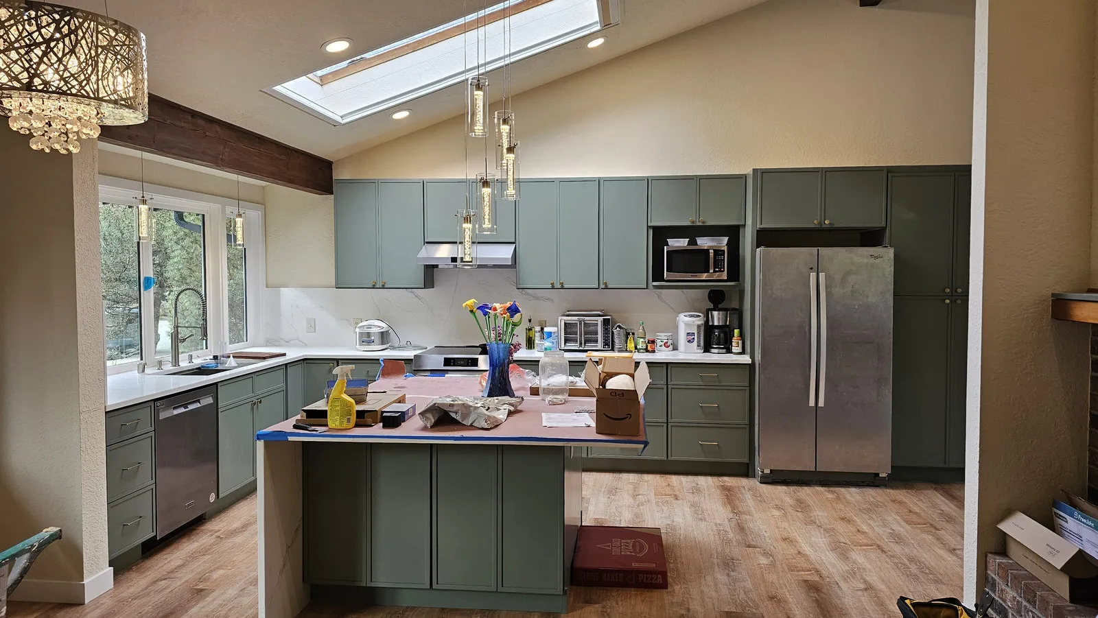 A finished sage-green shaker kitchen with a quartz island and pendant lighting under a skylight