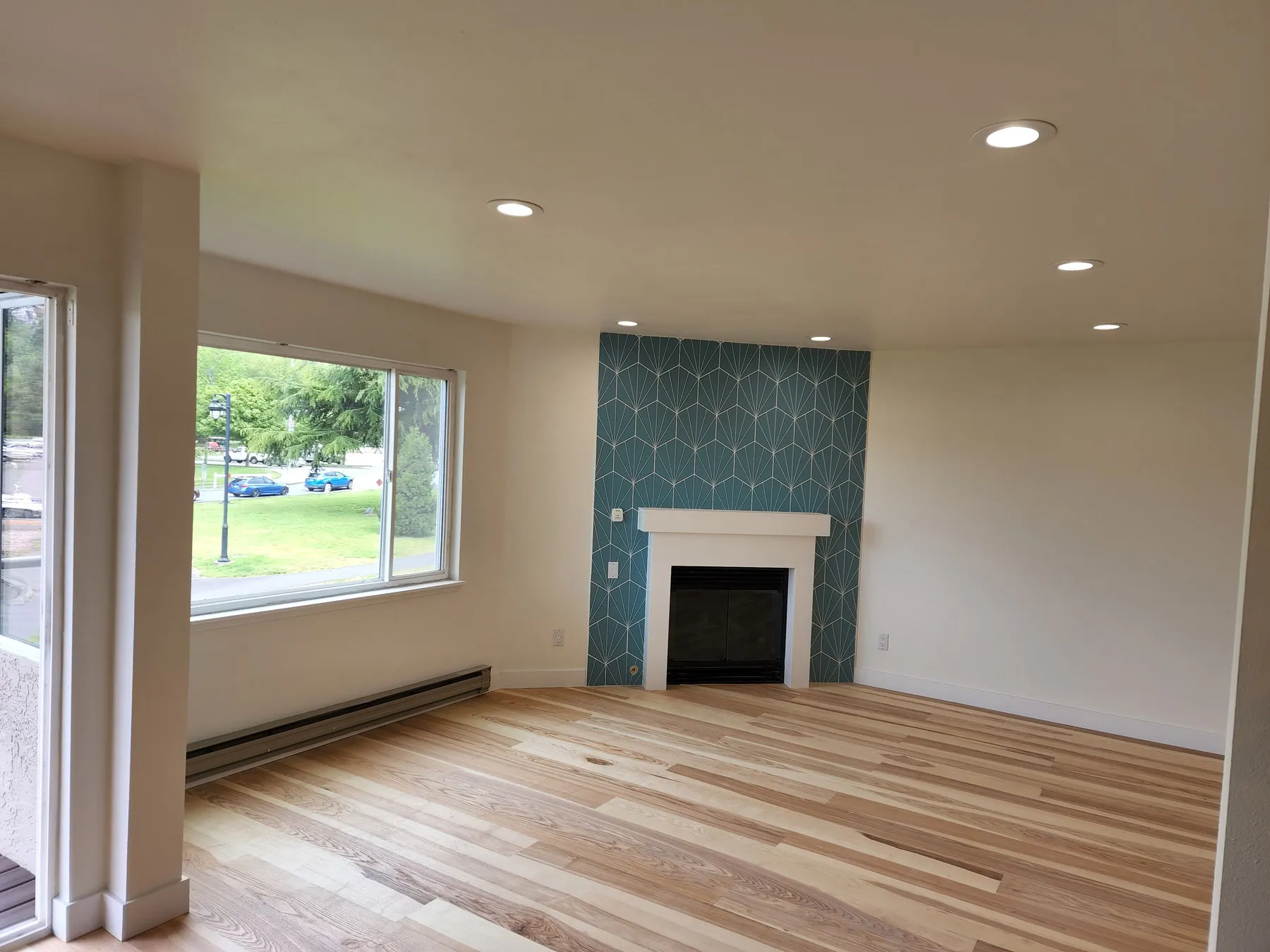 A hickory floor laid through a living room in Juanita, Kirkland, with a teal hex-tile fireplace surround